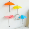 Three colorful umbrella-shaped wall hooks mounted on a wall, holding keys and small accessories, adding a playful touch to home decor.  