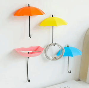 Three colorful umbrella-shaped wall hooks mounted on a wall, holding keys and small accessories, adding a playful touch to home decor.  