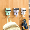 Cartoon cat hook with sunglasses, mounted on a wall, holding keys and accessories, adding a playful touch to home decor. 